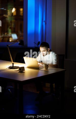 Thoughtful young businessman in glasses work on laptop at night preparing for startup presentation Stock Photo