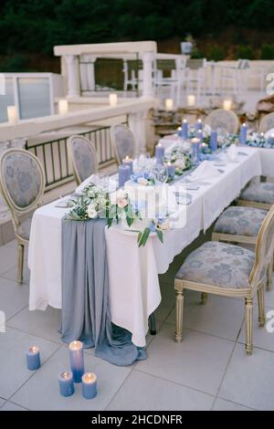 White bunk wedding cake decorated with flowers stands on a table with burning candles Stock Photo