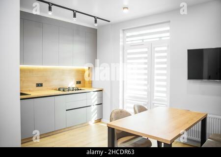 Wooden floor. Table with chairs. TV on the wall. Sunlight. Stock Photo