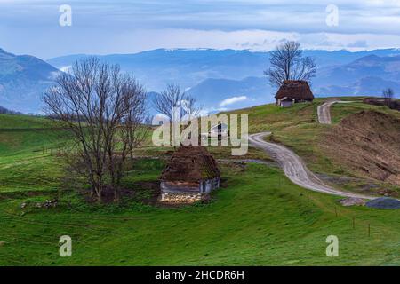 Traditional thatched huts against a picturesque skyscape with Trascau Mountains capped with snow. Photo taken on 30th of April 2021 in the old village Stock Photo