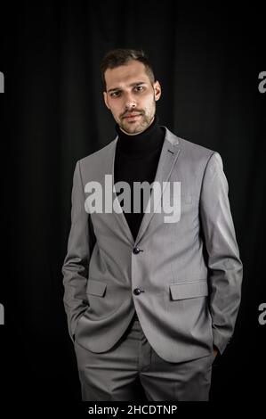 portrait of a young businessman in a gray suit and black turtleneck, looking serious with his hands in his pockets Stock Photo