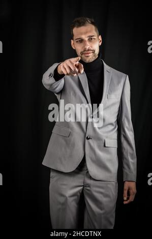 portrait of a young businessman in a gray suit and a black turtleneck, pointing his index finger in front of him Stock Photo