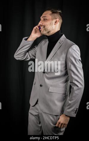 portrait of a young businessman with a gray suit and a black turtleneck, who is having a call on the mobile phone Stock Photo