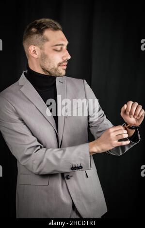 portrait of a young businessman in a gray suit and a black turtleneck, adjusting the sleeve of his jacket Stock Photo