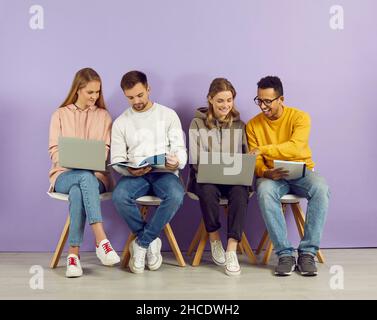 Happy college students sitting in line, working on laptops, and looking through study notes Stock Photo