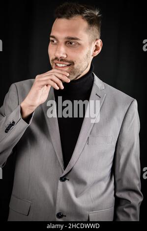portrait of a young businessman in a gray suit holding his chin with his fingers and seems to hesitate while he is pondering Stock Photo
