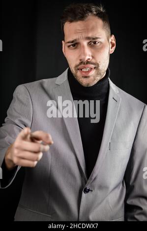 portrait of a young businessman in a gray suit and a black turtleneck, pointing his index finger in front of him Stock Photo