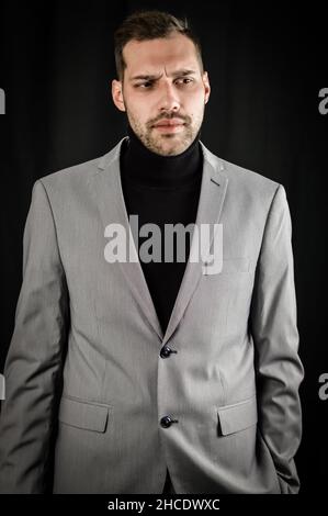 portrait of a young businessman in a gray suit and black turtleneck, looking serious with an hand in his pocket Stock Photo