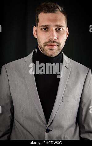 portrait of a young businessman in a gray suit and black turtleneck, looking serious, close up Stock Photo
