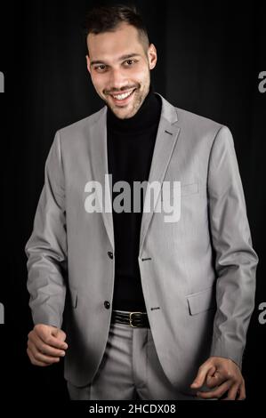portrait of a young businessman in a gray suit who smiles but shows some embarrassment with his hands Stock Photo