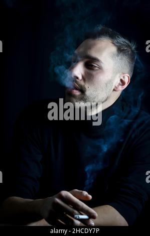 portrait of a young man who smokes a cigarette and is enveloped in swirls of smoke Stock Photo