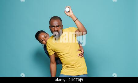 Man using flashlight for search and terrified woman hiding behind him in studio. Scared couple looking at scary thing and feeling nervous. Shocked people with anxious facial expression Stock Photo