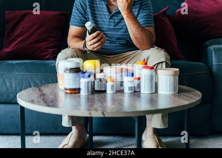 Concept of sick person with medical drugs. Fighting disease with medicines. Worried man with Medicine bottles on table. Stock Photo