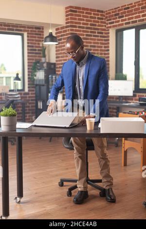 African american person gathering things in box after getting fired from business job. Frustrated person preparing to leave work after being discharged and dismissed by manager. Stock Photo