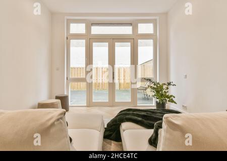 Interior design of contemporary light living room with white walls furnished with comfortable armchairs with pillows placed on carpet near poufs on pa Stock Photo