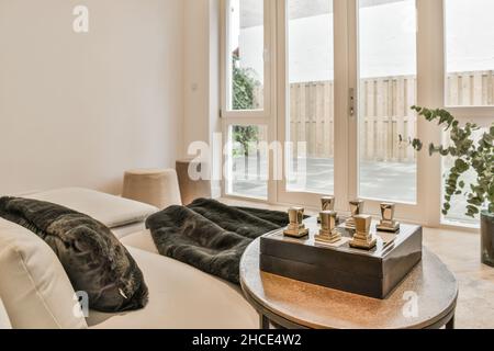 Interior design of contemporary light living room with white walls furnished with comfortable armchairs with pillows placed on carpet near poufs on pa Stock Photo