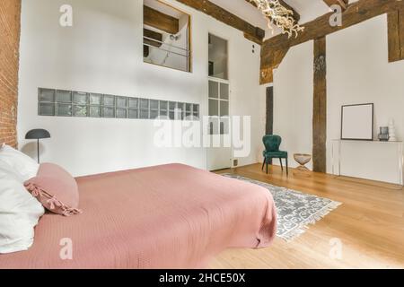 Comfortable bed with pillows and blanket placed near brick wall in spacious bedroom in daylight Stock Photo