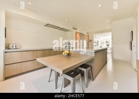 Interior on light spacious kitchen with modern appliances on wooden cupboards and fruit vase placed on dining table in modern apartment Stock Photo