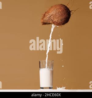 Milk pouring from fresh whole coconut into glass served on table against brown background Stock Photo