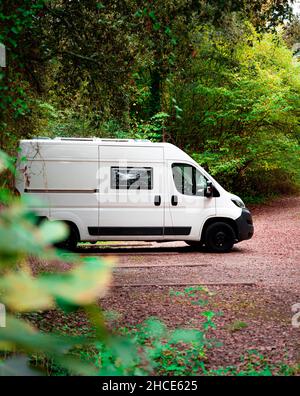 White minibus parked on path among green trees of lush woods in Catalonia in sunny day Stock Photo
