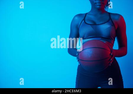 Confident African American female athlete holding basketball in blue light Stock Photo