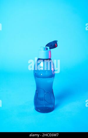 Opened plastic bottle of water placed against verdant background in studio in blue illumination Stock Photo