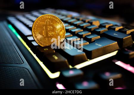 Round metal bitcoin coin placed on black keyboard of computer against blurred glowing monitor with numbers Stock Photo