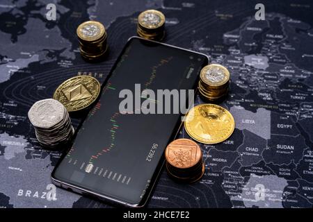 Stack of various bitcoins scattered on mobile phone display with financial chart on screen placed on world map Stock Photo