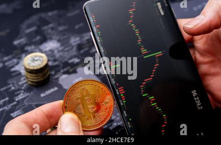 From above of hands of crop male holding bitcoin coin and mobile phone with financial chart on screen Stock Photo