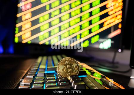 Round metal bitcoin coin placed on black keyboard of computer against blurred glowing monitor with numbers Stock Photo