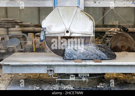 Large circle saw cutting block of black portoro marble placed on metal table in industrial factory Stock Photo