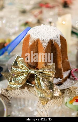 High angle of traditional Italian Pandoro dessert with icing sugar decorated with golden bow placed on table for Christmas dinner Stock Photo
