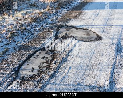 Dirt, unpaved road. It's a winter morning. The ground is covered with a layer of snow, the water in the puddle is frozen. Stock Photo