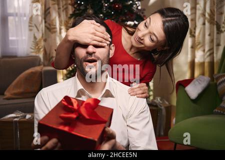 Surprised man receiving gift from his girlfriend on Christmas eve Stock Photo