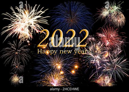 Happy new year 2022. Text and numer in golden colour with bright fireworks agianst dark sky in background.