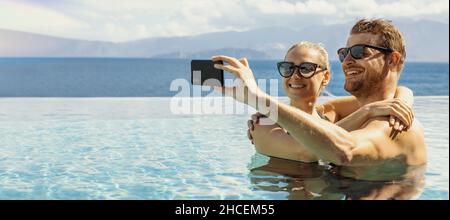 summer vacation - young happy couple taking selfie with phone in resort swimming pool. banner copy space Stock Photo