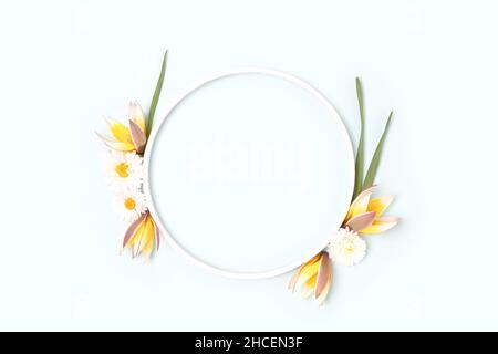 Round frame made of chamomile and wild tulip flowers on a blue pastel background. Stock Photo