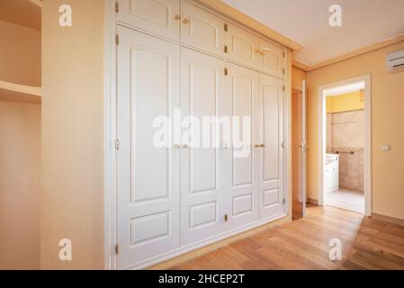 Bedroom with white walk-in closet and en-suite bathroom with parquet flooring Stock Photo