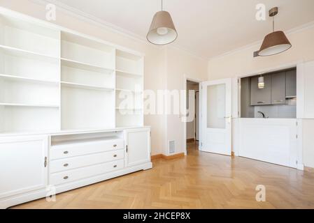 Living room with white lacquered wooden bookcase along with entrance to a kitchen with a herringbone parquet worktop Stock Photo
