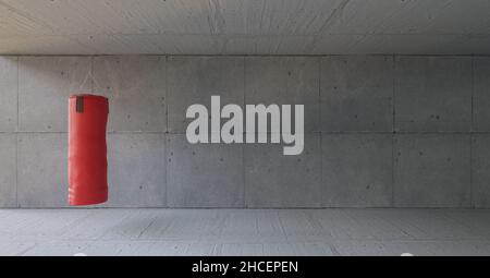 Red punching bag hangs in the gym in front of a concrete wall Stock Photo