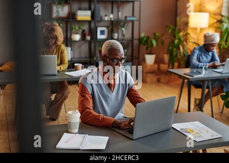 African young businessman typing on laptop at his workplace at office with his colleagues in the background Stock Photo
