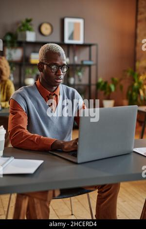 Serious African businessman in eyeglasses typing on laptop at his workplace at office Stock Photo