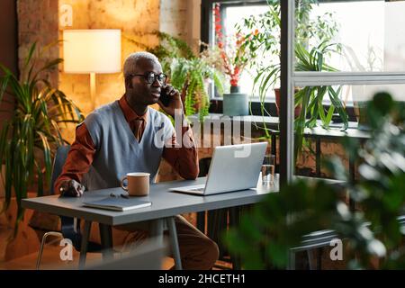 African businessman having a conversation on mobile phone while working at the table with laptop at office Stock Photo
