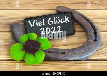 Lucky symbols horse shoe and clover with German Good Luck 2022 on wooden background Stock Photo