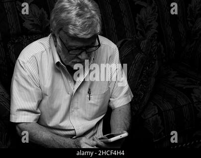 Black and White photo of an old man messing with a phone Stock Photo