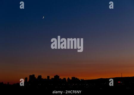 A crescent moon hangs above the silhouetted Montreal skyline after sunset, Quebec, Canada Stock Photo