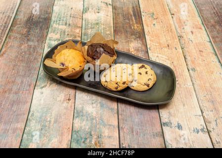 Cookies and muffins for breakfast or snack on black tray and wooden table Stock Photo