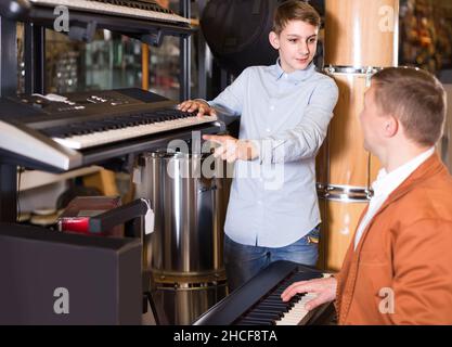 Father and teenage son examining keyboards in guitar shop Stock Photo