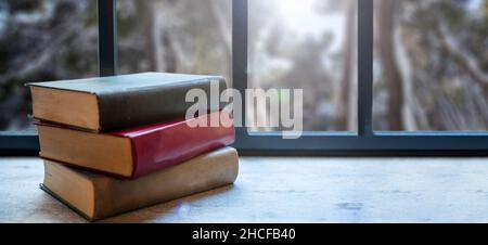 Books stack on a window sill. Closed old notebooks closeup view. Home interior background, reading and relaxation Stock Photo