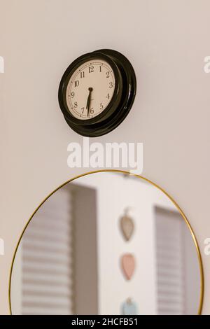 Black vintage clock and circular mirror with gold frame on the white wall. Stock Photo